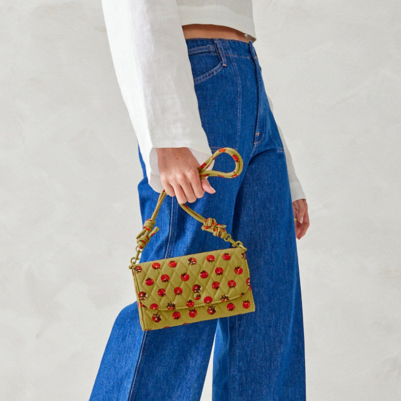 model holding green crossbody wallet purse with tomato pattern against denim pants