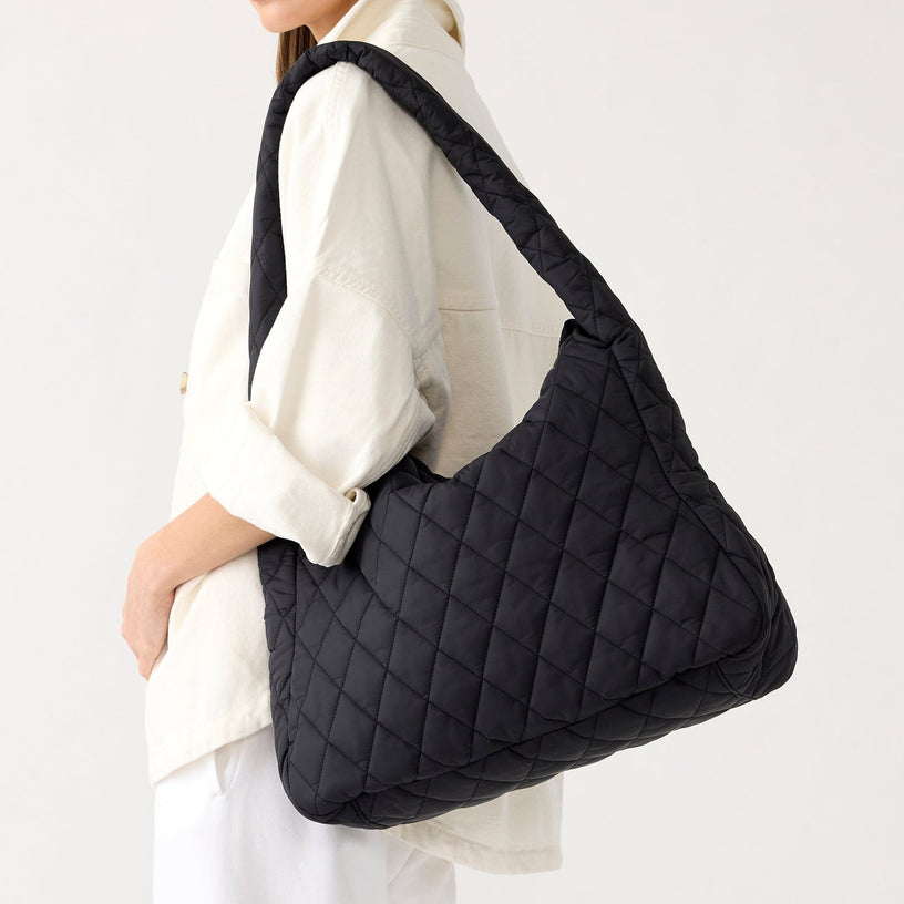 model wearing white white jacket with large black quilted hobo tote bag over her shoulder